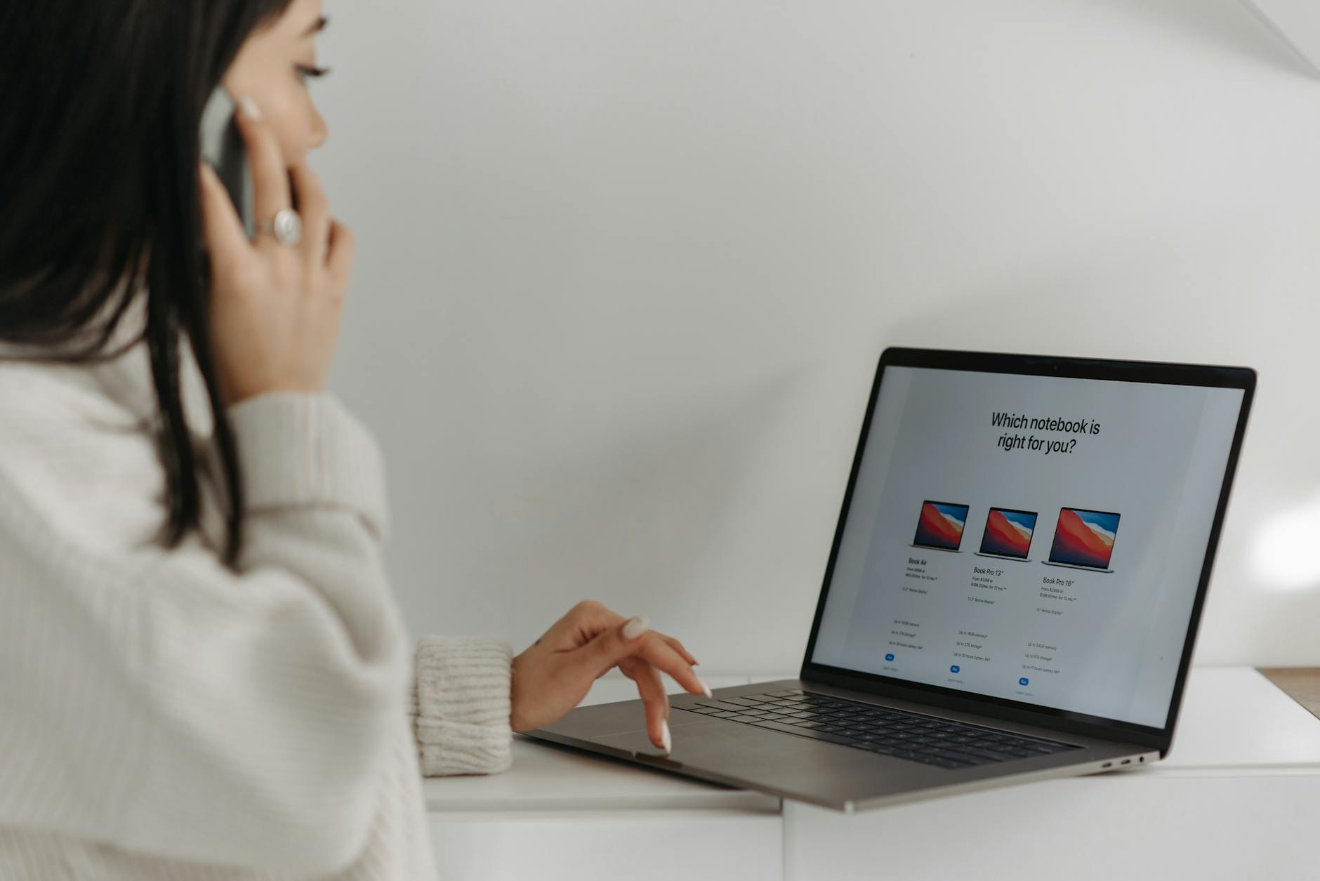 Azjatka z telefonem i laptopem na tle białej ściany podczas zakupów online