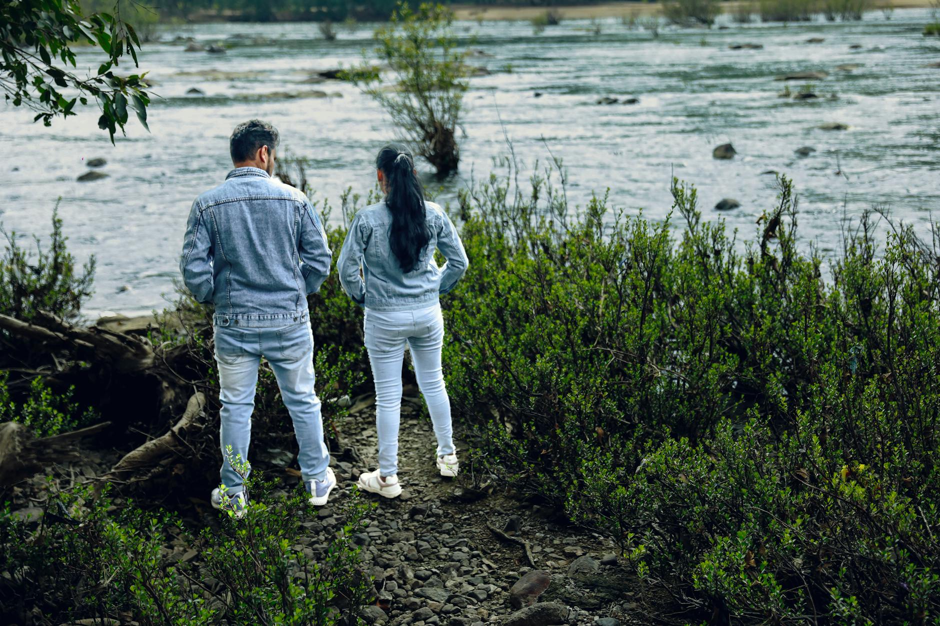 Para w dżinsowych kurtkach spaceruje nad zielonym brzegiem Renu