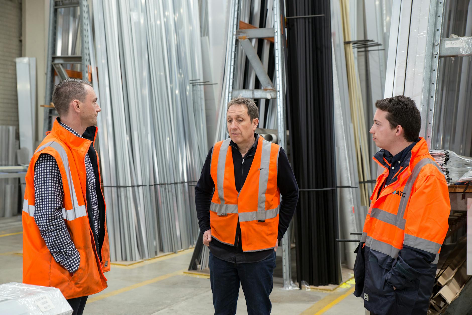 Zespół w kamizelkach odblaskowych rozmawia w hali przemysłowej