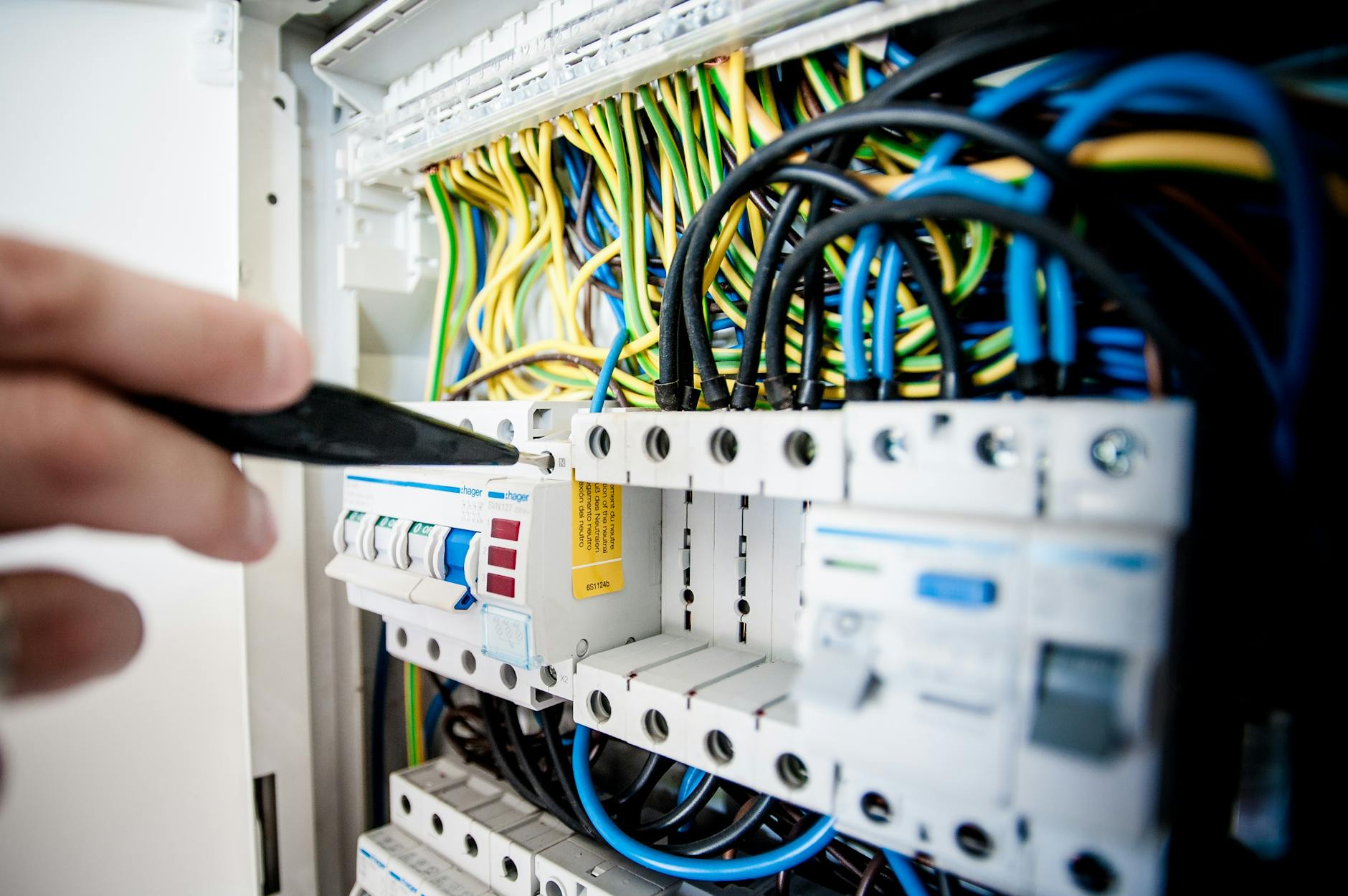 Elektryk podłącza kolorowe przewody w domowej rozdzielnicy z wyłącznikami