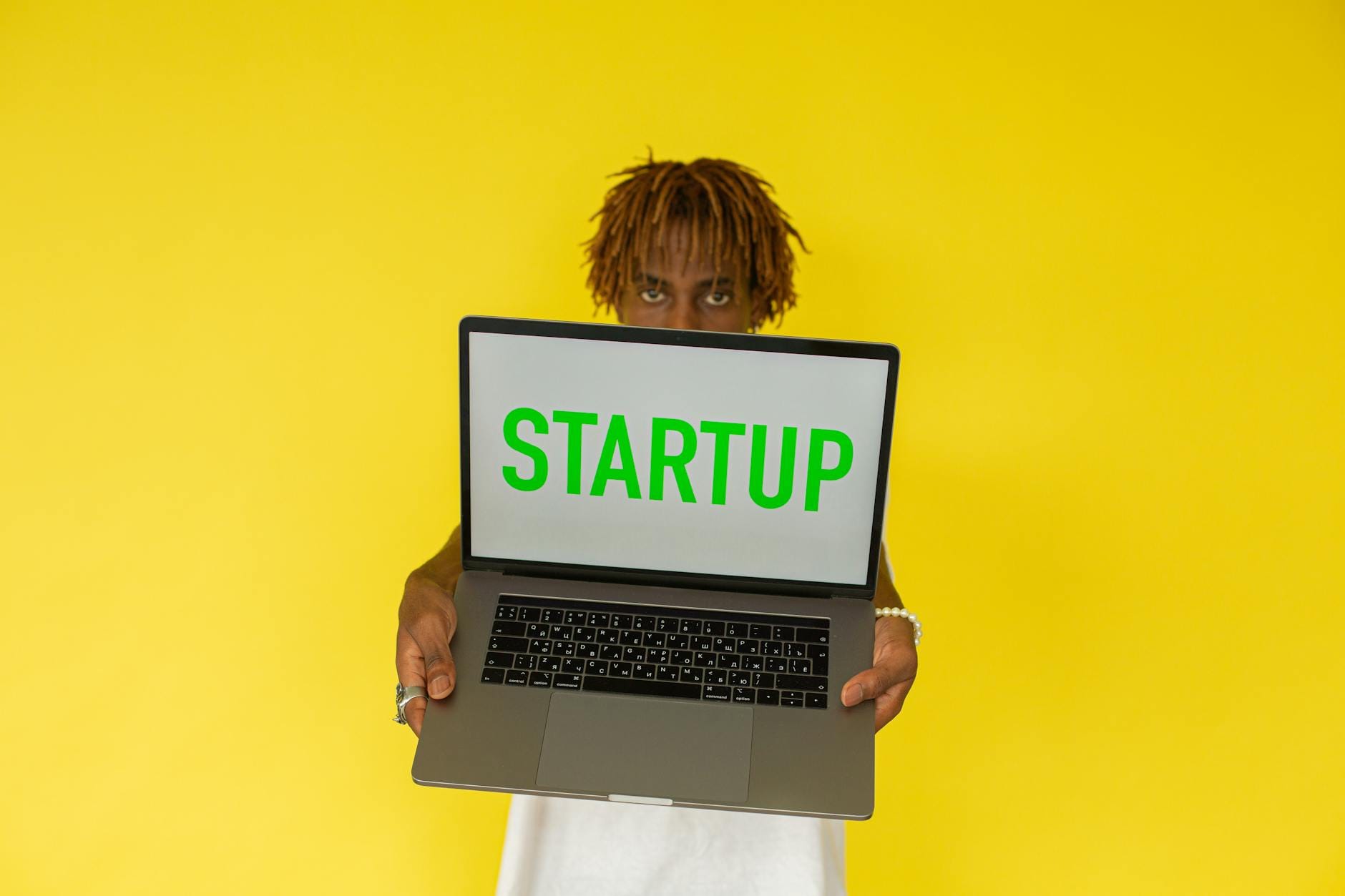 Młody mężczyzna trzyma laptop z napisem Startup na żółtym tle