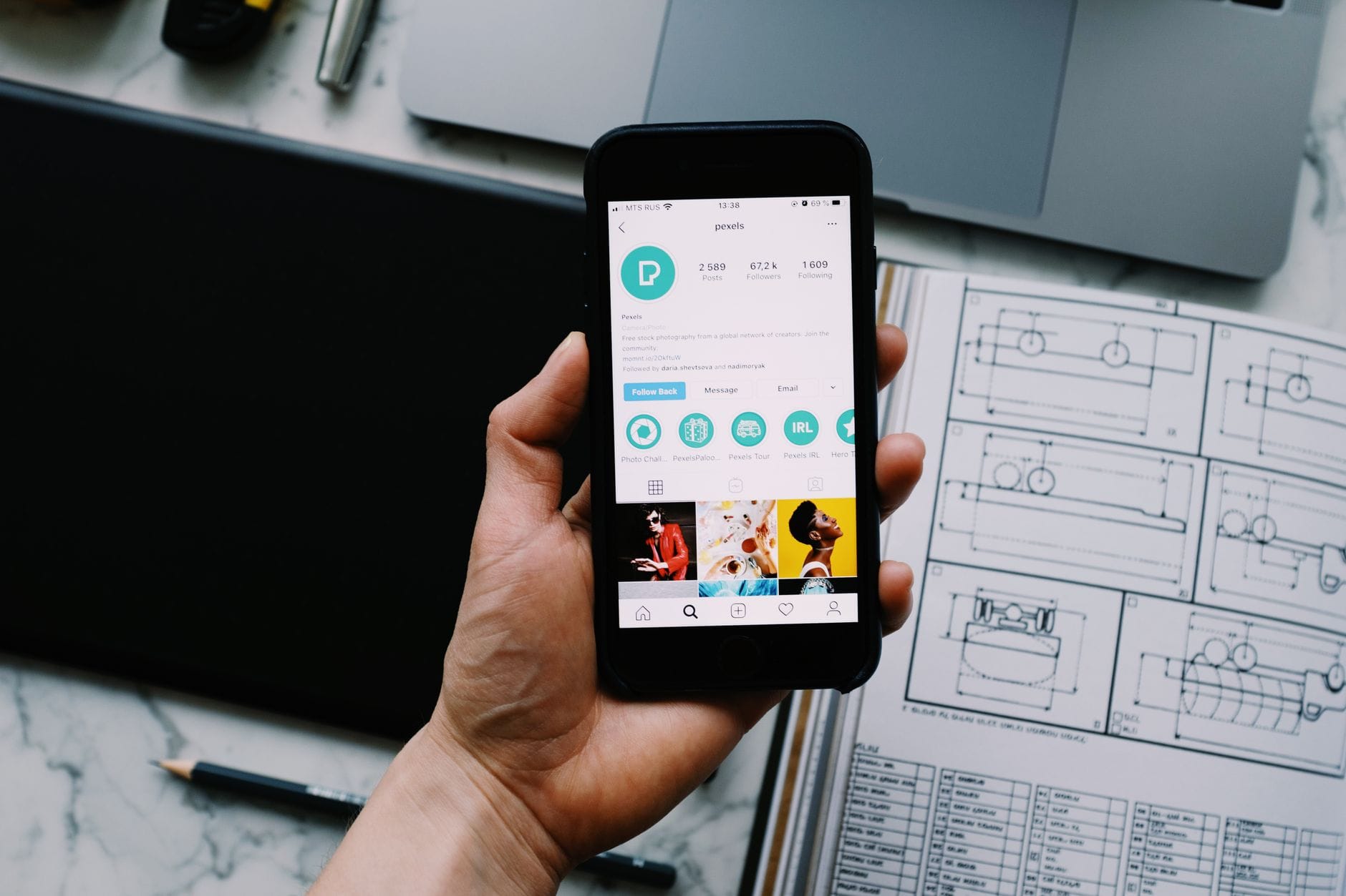 Dłoń trzyma smartfon z profilem społecznościowym obok gadżetów na biurku