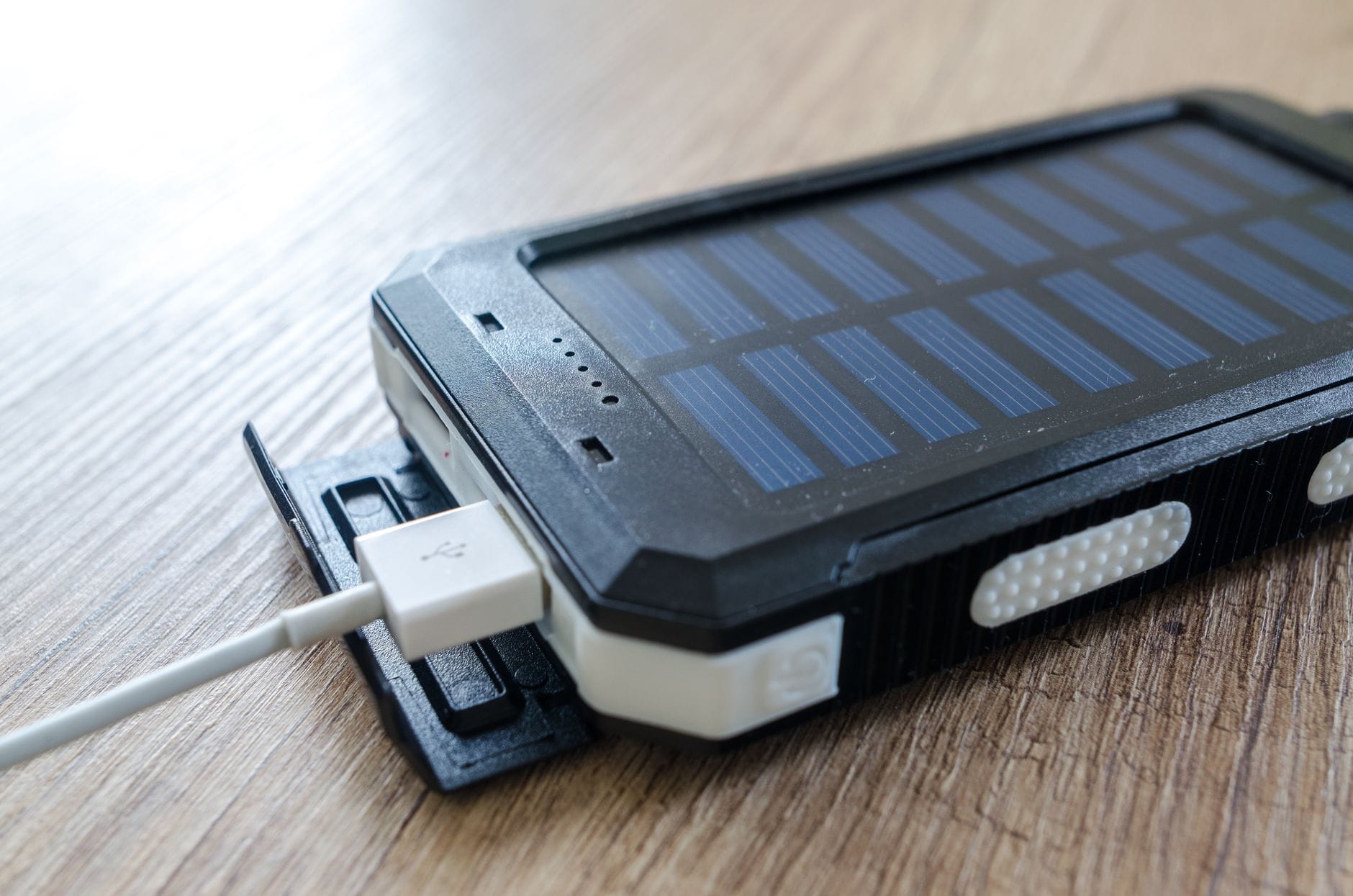Zbliżenie przenośnej ładowarki solarnej z kablem USB na drewnianym blacie