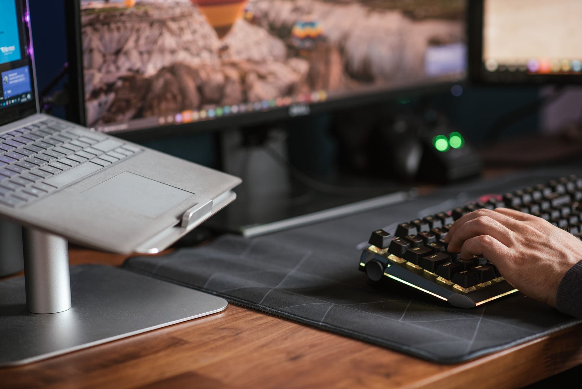 Mężczyzna piszący na podświetlanej klawiaturze obok laptopa na stojaku